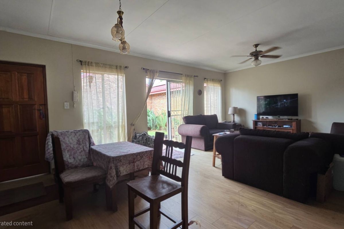 A spacious living room featuring laminate flooring, a ceiling fan, and sliding glass doors that provide access to the outdoor area.