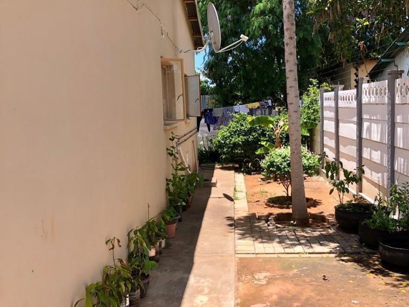 Rear exterior view of the apartment showing a paved walkway, precast boundary wall, and visible cracks on the exterior wall plaster.