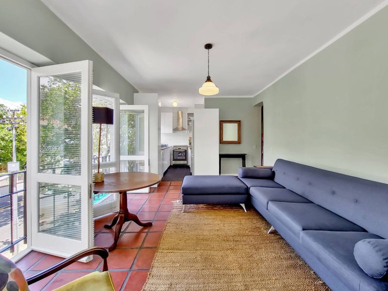 Open-plan living area featuring terracotta flooring, flowing into a functional kitchen with built-in cabinetry and direct access to a balcony.
