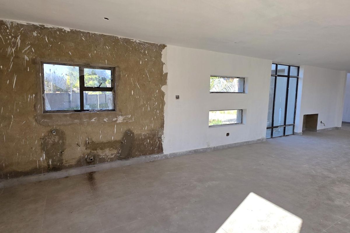 An empty, unfinished living area featuring tiled floors, aluminium windows, and a built-in fireplace, currently requiring plastering and final interior finishes.