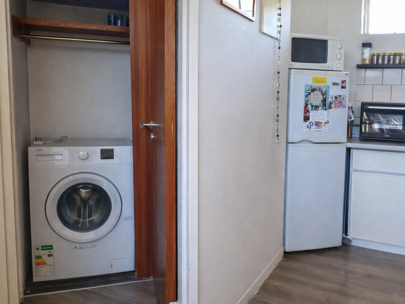 A functional laundry nook featuring built-in shelving and a hanging rail, adjacent to a compact kitchen area with tiled backsplash.