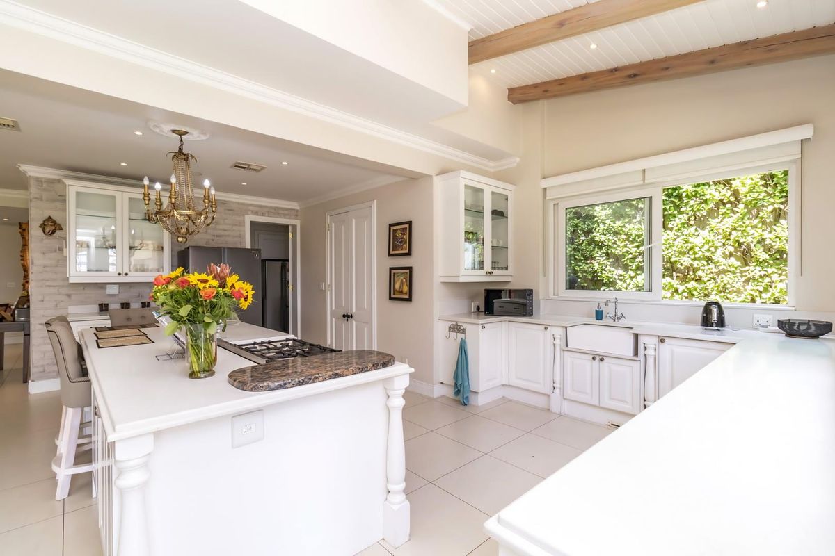 Spacious kitchen featuring white cabinetry, a large central island with a gas hob, farmhouse sink, and exposed timber ceiling beams.