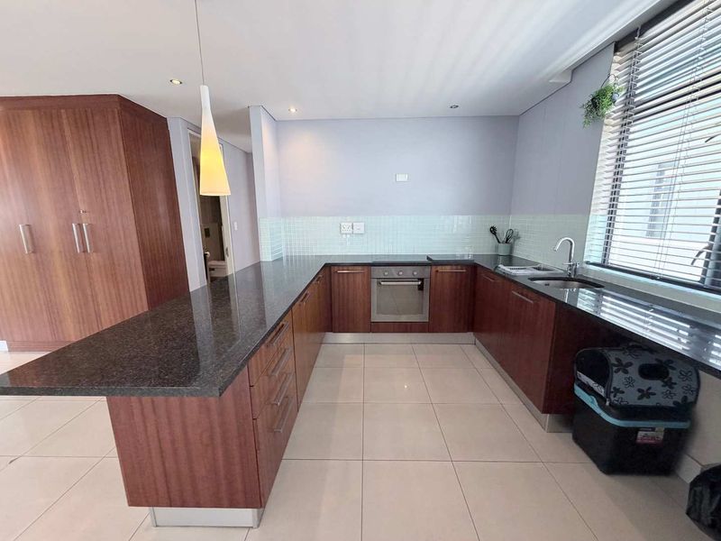 Modern kitchen featuring dark granite countertops, wood-veneer cabinetry, built-in oven, hob, and a tiled backsplash with ample workspace and natural light.