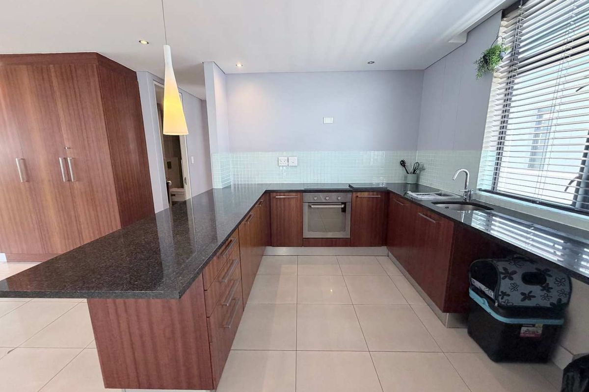 Modern kitchen featuring dark granite countertops, wood-veneer cabinetry, built-in oven, hob, and a tiled backsplash with ample workspace and natural light.