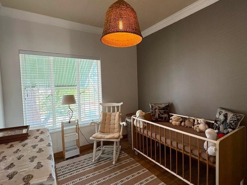 A well-maintained bedroom featuring warm timber flooring, crown molding, and natural light through venetian blinds.
