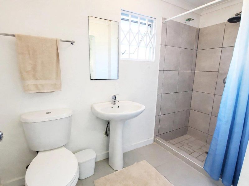 A functional bathroom featuring a pedestal basin, a tiled shower enclosure, and a window with security bars.