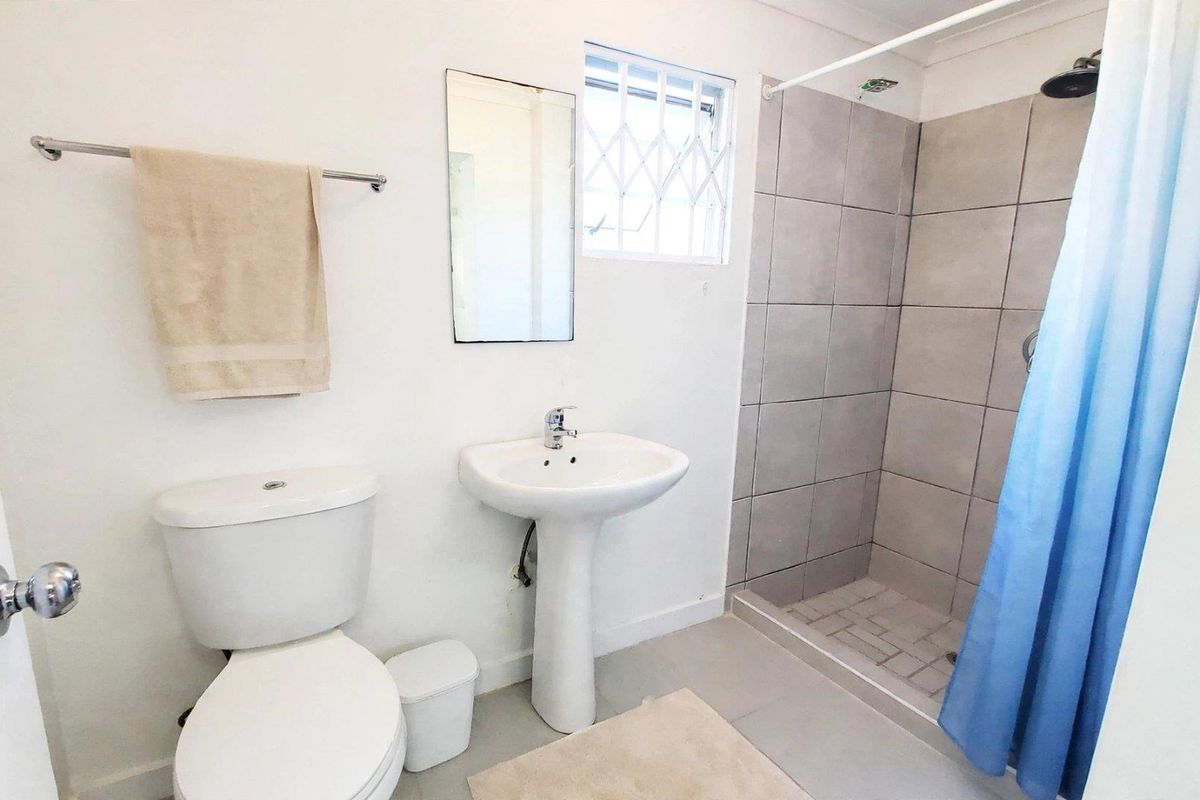 A functional bathroom featuring a pedestal basin, a tiled shower enclosure, and a window with security bars.