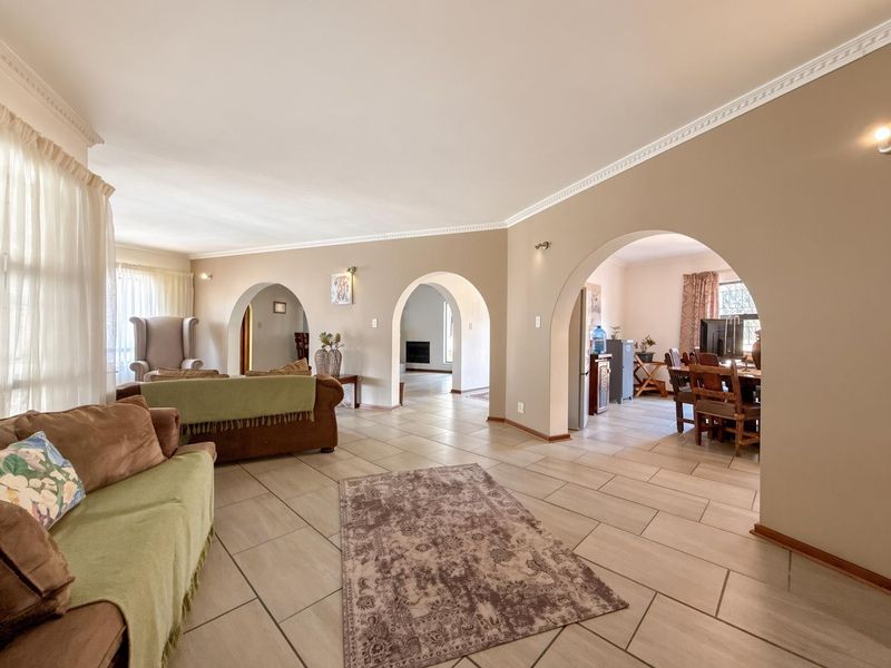Spacious open-plan living area featuring distinctive arched doorways, ceramic tile flooring, and decorative crown molding, creating a connected and flowing interior layout.