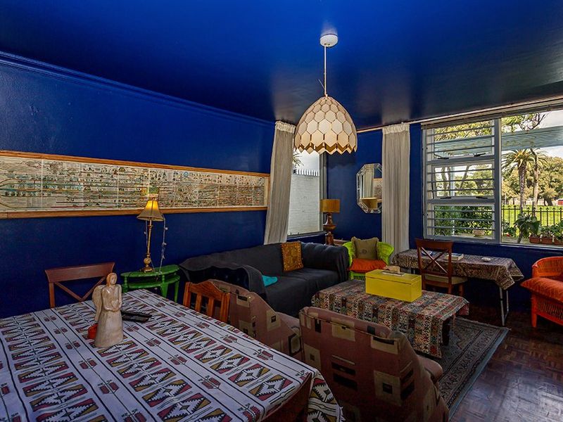A spacious living room featuring classic parquet flooring, a large window providing natural light, and a bold blue ceiling and wall finish.