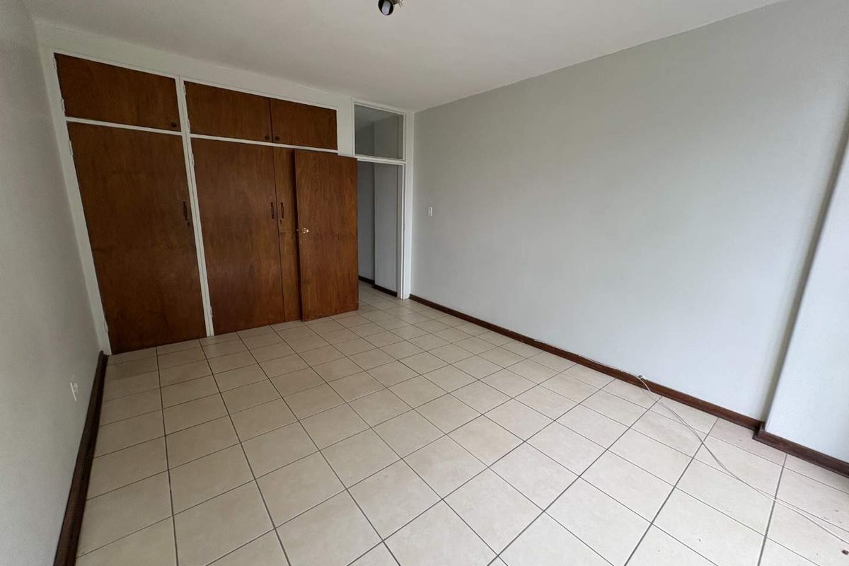 An empty bedroom featuring tiled flooring and built-in wooden cupboards, offering a blank canvas for personalization.