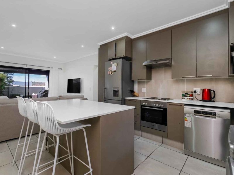 Modern open-plan kitchen featuring a central island, sleek cabinetry, and integrated appliances, seamlessly flowing into the adjacent living area with access to the patio.