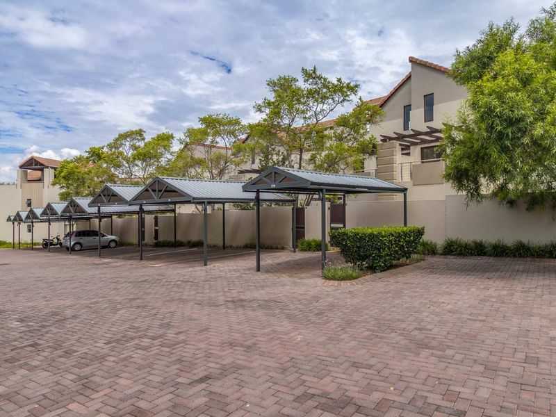 A well-maintained apartment complex exterior featuring paved driveway access and covered parking bays for residents.