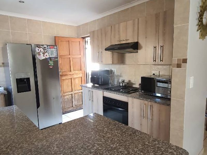 A functional kitchen featuring granite countertops, built-in oven, hob, extractor fan, and tiled backsplash with ample cabinetry.