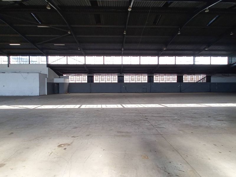 Spacious industrial warehouse featuring high ceilings, exposed steel trusses, concrete flooring, and large clerestory windows providing ample natural light.