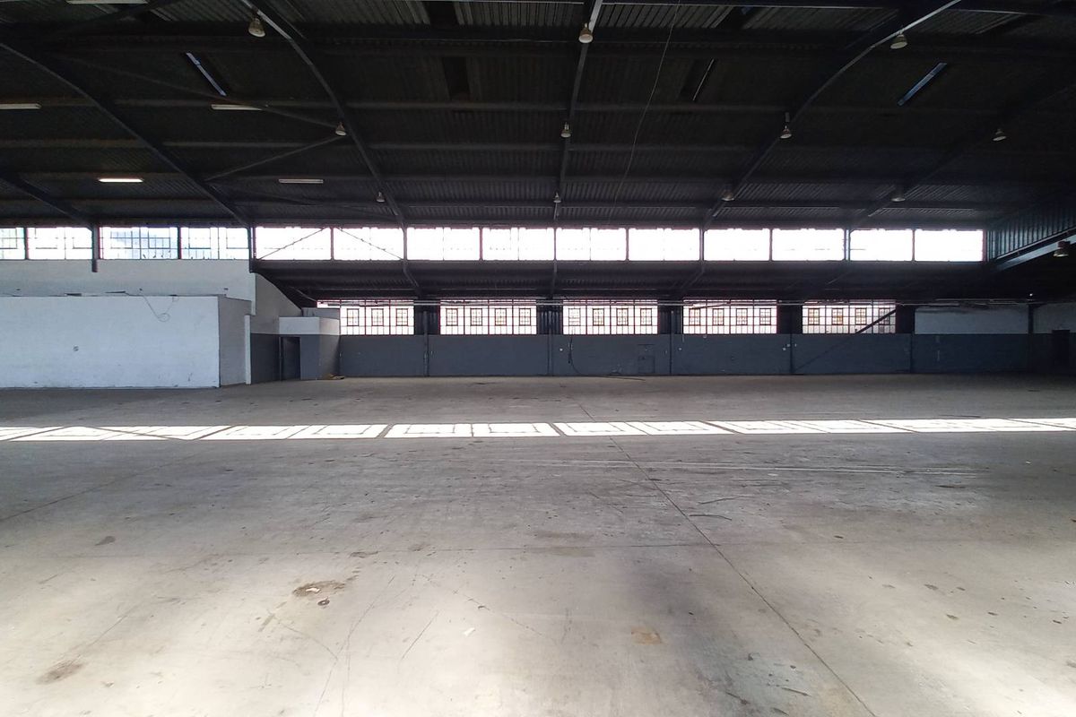 Spacious industrial warehouse featuring high ceilings, exposed steel trusses, concrete flooring, and large clerestory windows providing ample natural light.