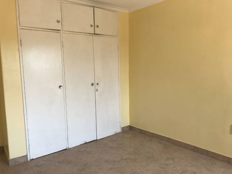 An empty bedroom featuring tiled flooring and built-in cupboards with overhead storage compartments.