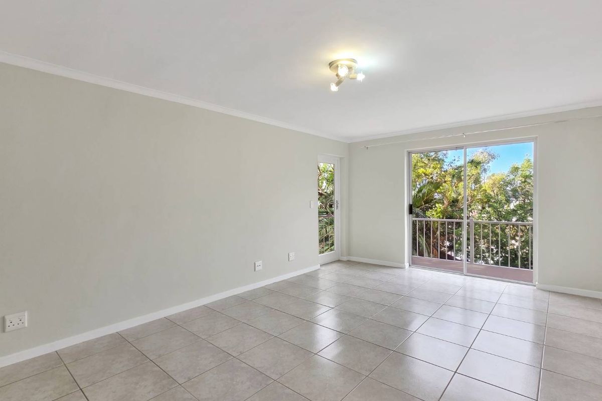 A bright, empty living room featuring neutral tiled flooring, a ceiling light fixture, and sliding glass doors leading to a private balcony.