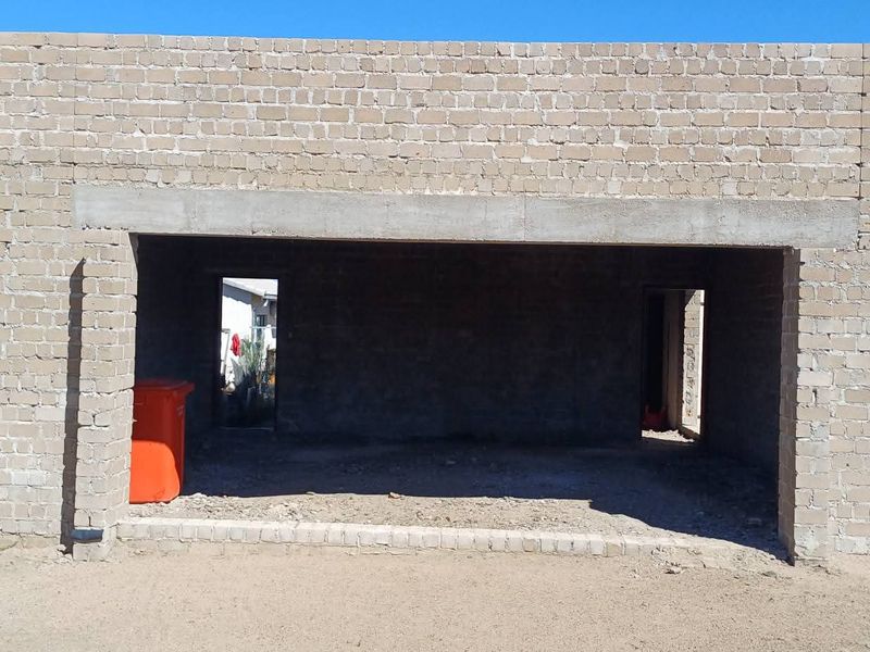 An unfinished garage structure featuring exposed brickwork and a concrete lintel, currently in the early stages of construction.