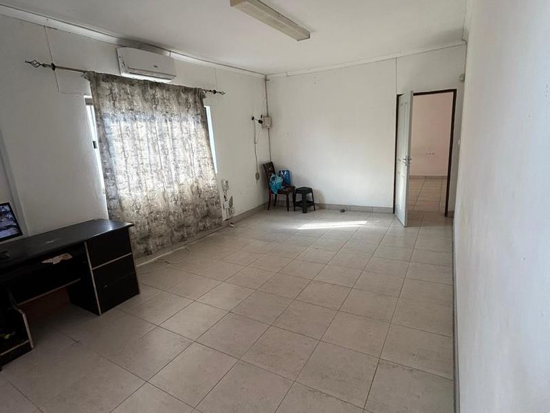 A spacious, neutrally finished living area featuring tiled flooring, a wall-mounted air conditioning unit, and direct access to an adjoining room.