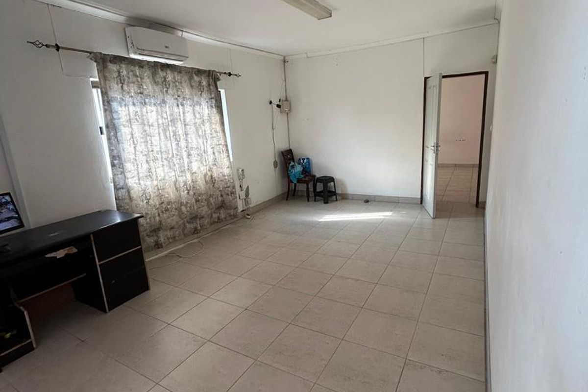 A spacious, neutrally finished living area featuring tiled flooring, a wall-mounted air conditioning unit, and direct access to an adjoining room.