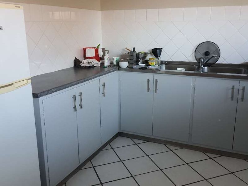 A functional kitchen featuring laminate countertops, a stainless steel sink, tiled backsplash, and ample built-in cabinetry with ceramic floor tiles.