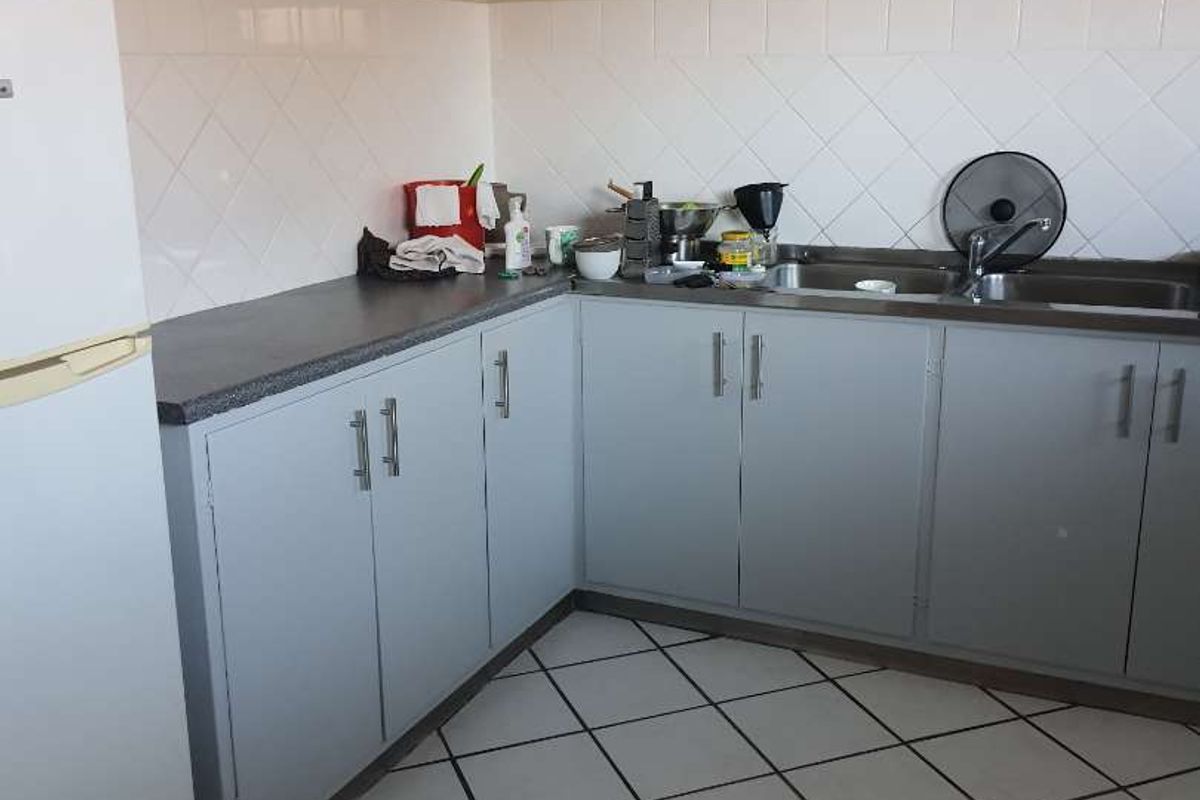 A functional kitchen featuring laminate countertops, a stainless steel sink, tiled backsplash, and ample built-in cabinetry with ceramic floor tiles.