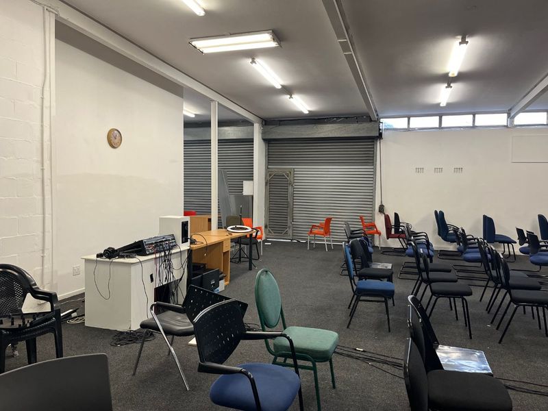 A spacious open-plan commercial or multi-purpose area featuring industrial-style roller shutter doors, fluorescent lighting, and carpeted flooring, suitable for various business or event uses.