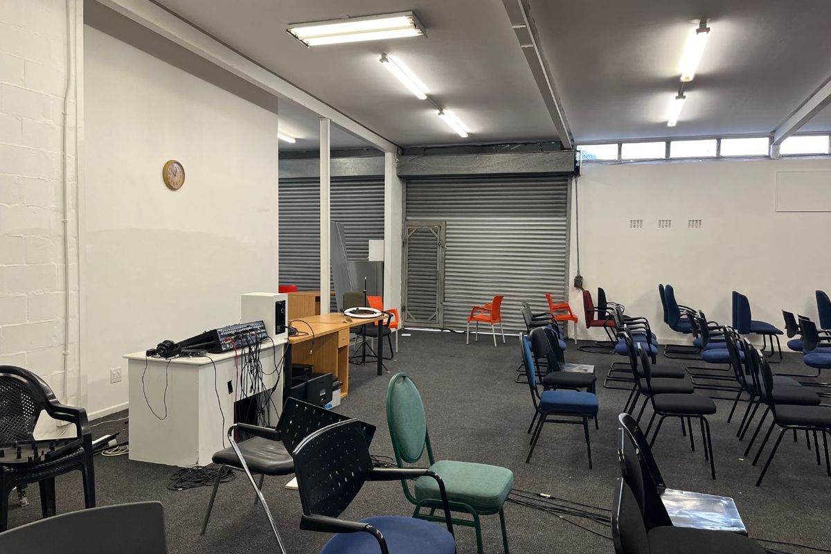 A spacious open-plan commercial or multi-purpose area featuring industrial-style roller shutter doors, fluorescent lighting, and carpeted flooring, suitable for various business or event uses.