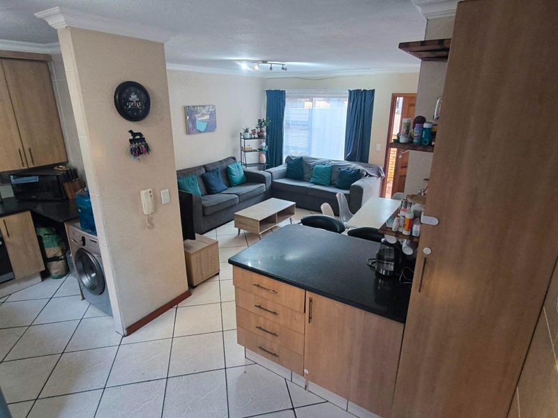 Open-plan living area featuring a functional kitchen with built-in cabinetry, hob, and oven, seamlessly flowing into a comfortable lounge space with tiled flooring.