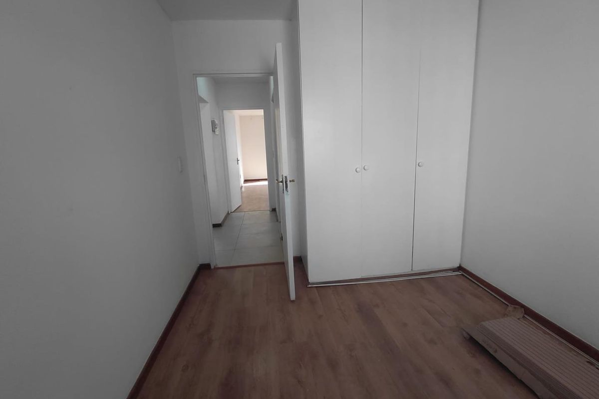 An empty bedroom featuring laminate flooring and a built-in wardrobe, with a doorway leading to an adjacent hallway.