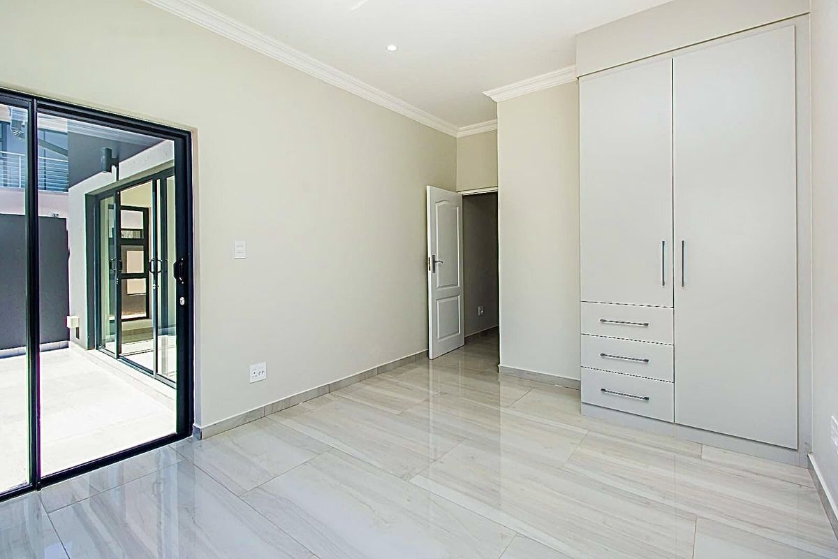 A bright, modern bedroom featuring polished tile flooring, built-in cabinetry, and sliding glass doors providing direct access to an outdoor patio area.