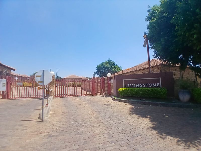 The entrance to Livingstone complex featuring a secure gated access point, brick paved driveway, and perimeter walling with electric fencing.