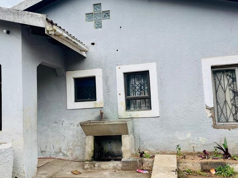 Rear exterior view of the property featuring a concrete wash basin, security bars on windows, and a textured plaster finish requiring maintenance.