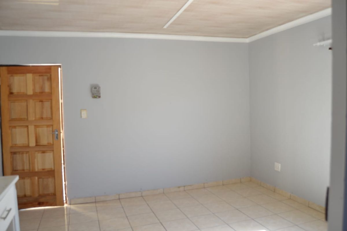 An empty living area featuring tiled flooring, a wooden panel door, and neutral grey walls, ready for personalization.