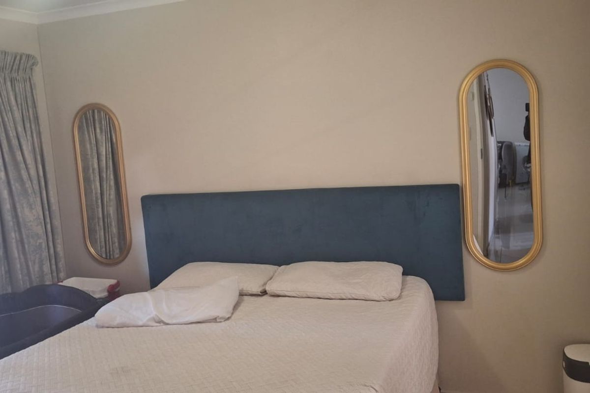 A bedroom featuring neutral wall tones, a blue upholstered headboard, and two wall-mounted oval mirrors.