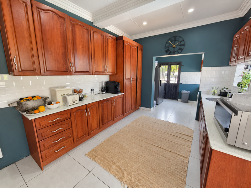 A well-maintained kitchen featuring warm wooden cabinetry, white subway tile backsplash, stone countertops, and modern recessed lighting with an adjacent scullery area.