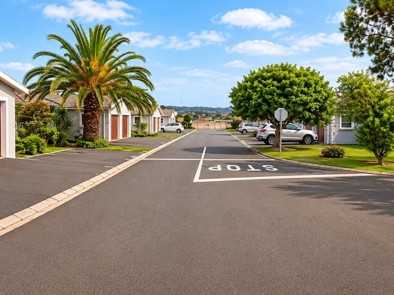 A well-maintained residential street view within an apartment complex, featuring paved roads, landscaped greenery, and clear access to garage units.