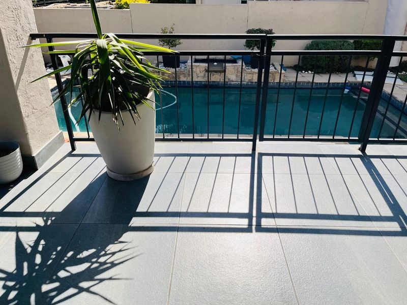 A tiled balcony area featuring a metal balustrade overlooking a private swimming pool and garden area.