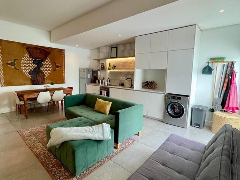 Modern open-plan living area featuring a compact kitchen with built-in cabinetry, integrated laundry appliance, and neutral tiled flooring throughout.