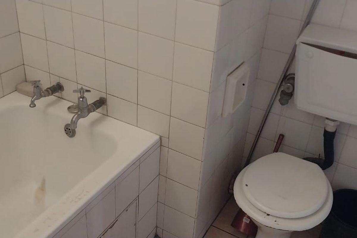A dated bathroom featuring a standard bathtub with wall-mounted taps and a close-coupled toilet with a high-level cistern.