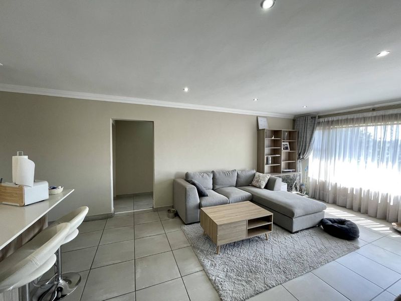 Spacious open-plan living area featuring neutral tiled flooring, recessed downlighting, and a functional breakfast bar, creating a bright and versatile living space.