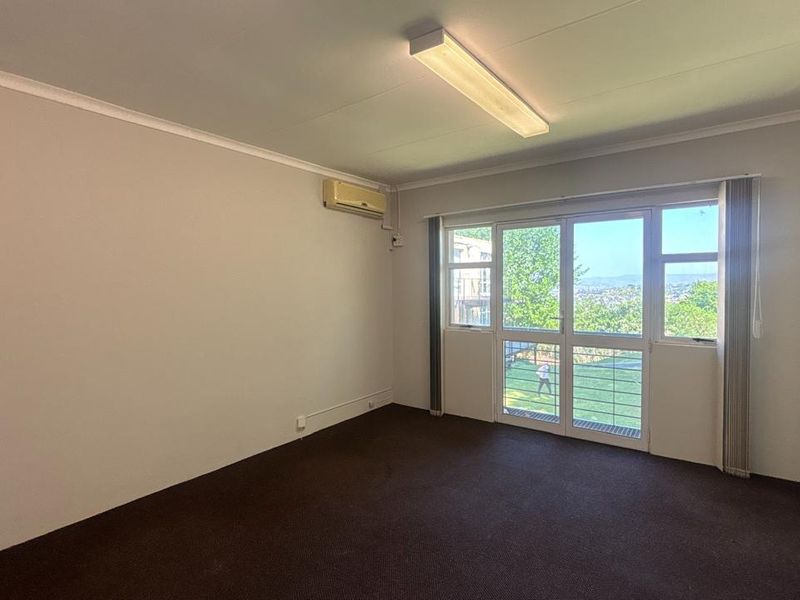 A bright, empty office space featuring carpeted flooring, an integrated air conditioning unit, and a sliding glass door providing natural light and outdoor views.