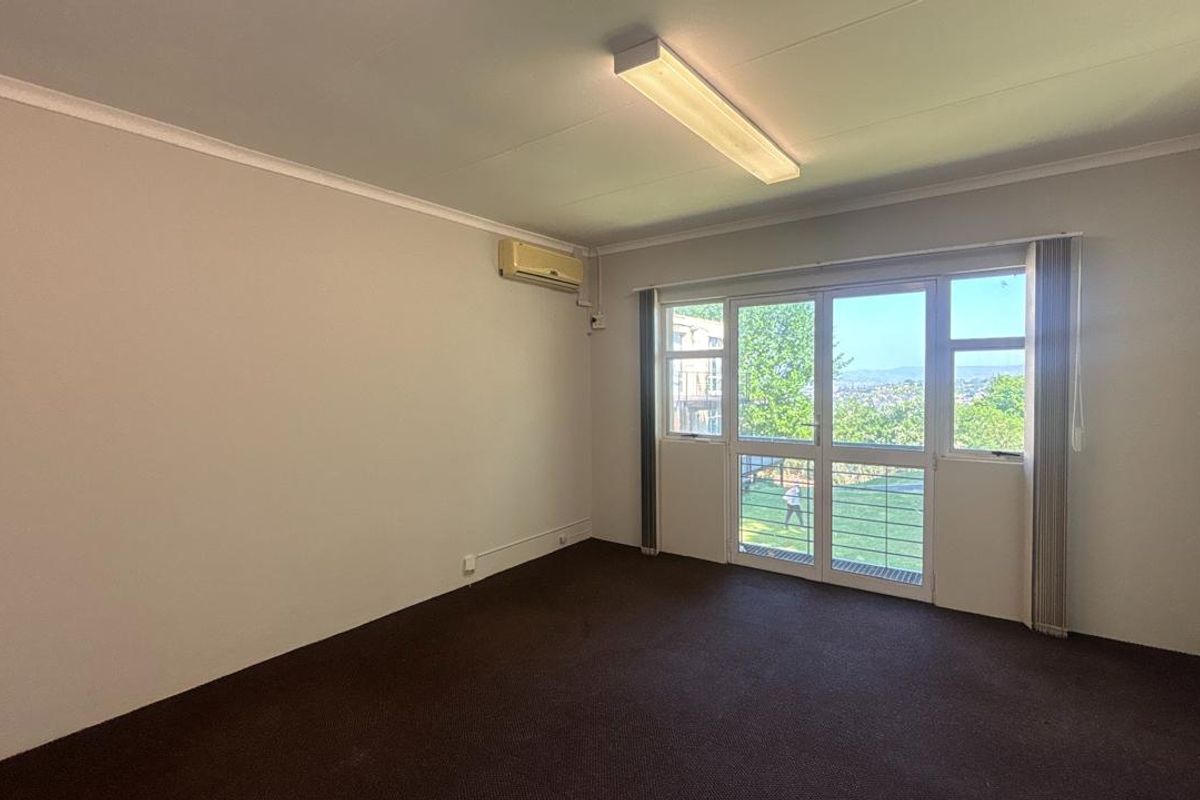 A bright, empty office space featuring carpeted flooring, an integrated air conditioning unit, and a sliding glass door providing natural light and outdoor views.