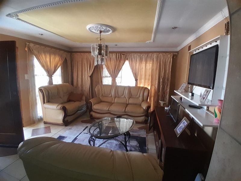 A comfortable living room featuring decorative ceiling detailing, a central chandelier, and a built-in wall shelving unit for media storage.