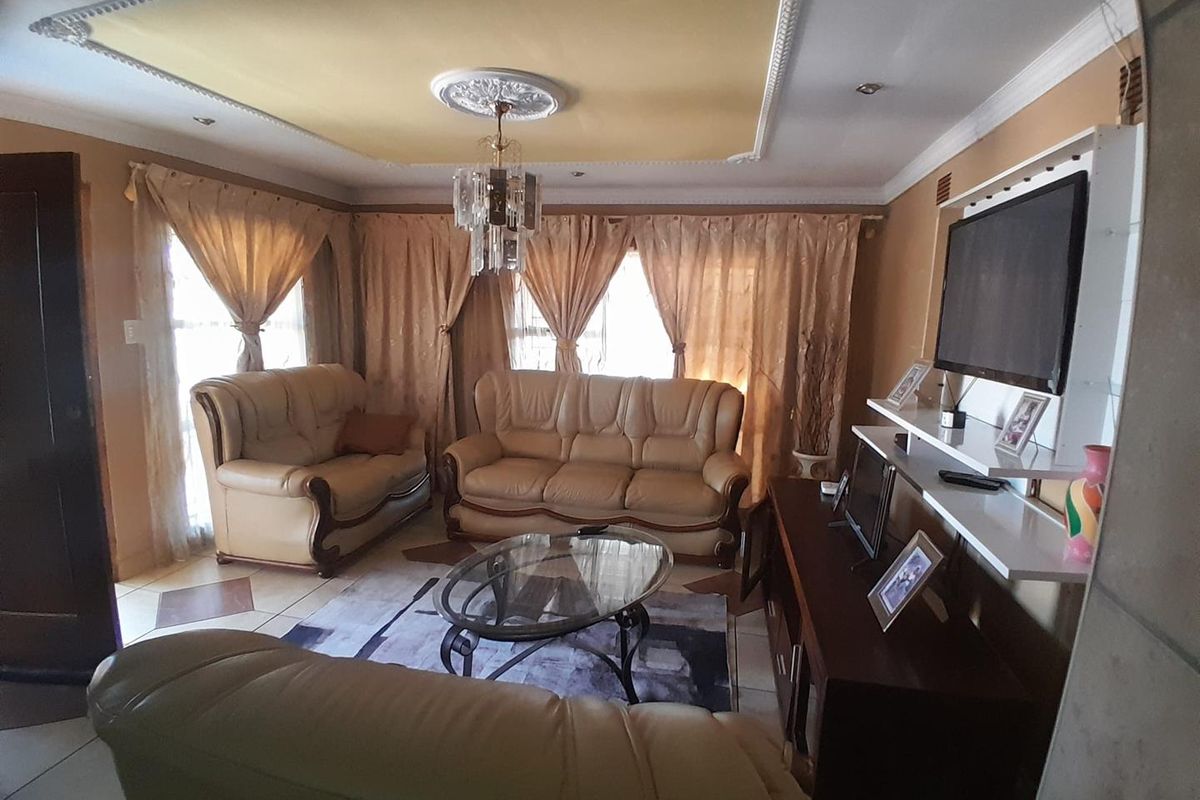 A comfortable living room featuring decorative ceiling detailing, a central chandelier, and a built-in wall shelving unit for media storage.