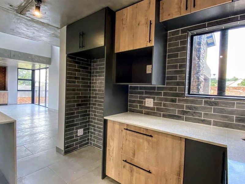 Modern open-plan kitchen featuring sleek wood-tone cabinetry, stone countertops, subway tile backsplash, and an exposed concrete ceiling, flowing into a spacious living area.