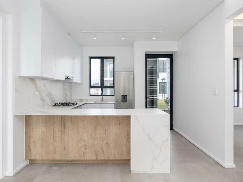 Modern kitchen featuring sleek white and wood-grain cabinetry, stone countertops with marble-look splashback, gas hob, and integrated track lighting in a clean, open space.