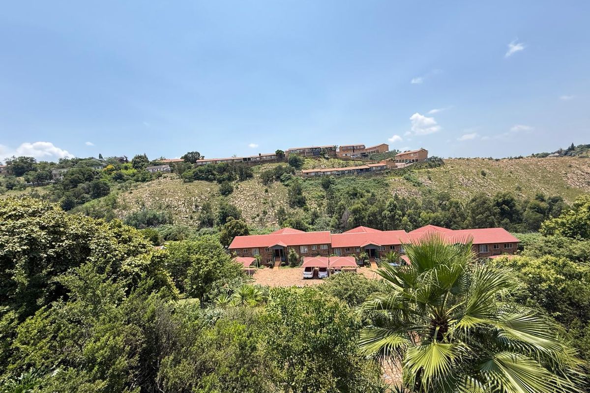 An elevated aerial view of a residential apartment complex featuring red tiled roofs and covered parking areas set within a lush, hilly landscape.