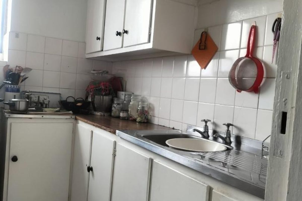 A compact, dated kitchen featuring white built-in cabinetry, a stainless steel sink, and tiled backsplash, offering potential for a modern renovation.