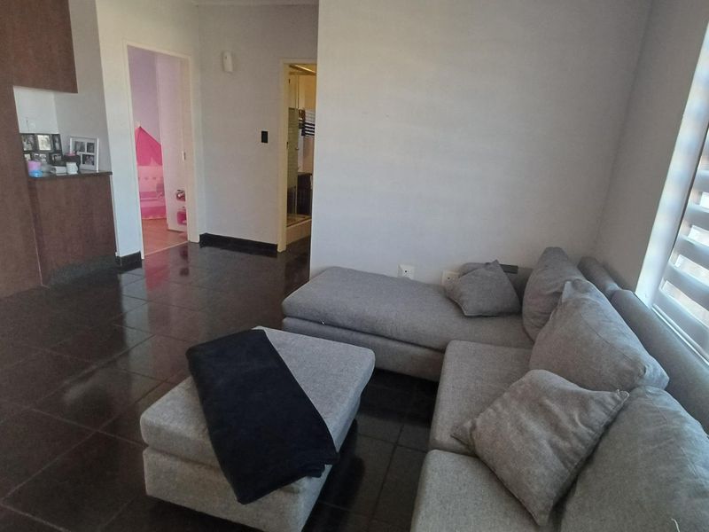 A living room area featuring dark tiled flooring and modern venetian blinds, providing access to adjacent rooms within the apartment.